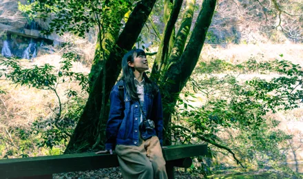 Eine junge Frau sitzt auf einer Bank in einem Wald und genießt die Natur während des Waldbadens.
