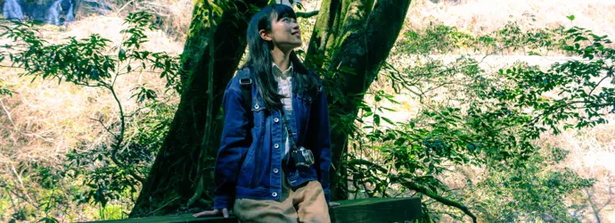 Eine junge Frau sitzt auf einer Bank in einem Wald und genießt die Natur während des Waldbadens.