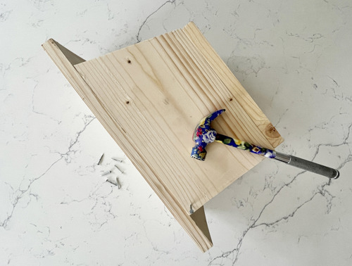 Tavole di legno assemblate con chiodi e martello durante la costruzione di una casetta per uccelli.