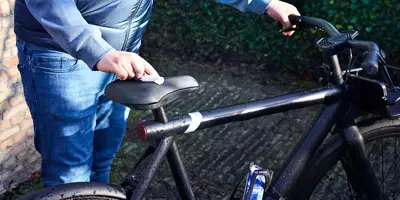 Een jonge man maakt het zadel van zijn fiets schoon in een tuin terwijl de zon schijnt.