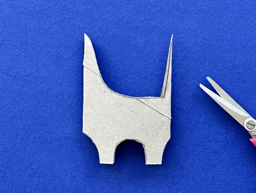 Rotolo di carta igienica tagliato a forma di dinosauro giace su sfondo blu con accanto un paio di forbici a punta.