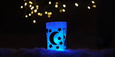 Eine mit Sternen und einem Mond dekorierte selbst gebastelte Papierlaterne scheint in blauem Licht.