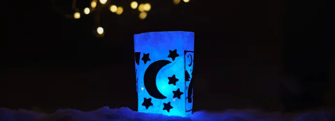 Eine mit Sternen und einem Mond dekorierte selbst gebastelte Papierlaterne scheint in blauem Licht.