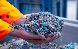 Foto in primo piano di mani a coppino che tengono coriandoli colorati di plastica riciclata.