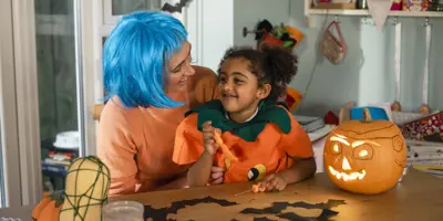 Ein verkleidetes Kind auf dem Schoß einer erwachsenen Person, umgeben von selbst gebastelter Halloween Deko.