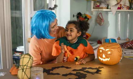 Ein verkleidetes Kind auf dem Schoß einer erwachsenen Person, umgeben von selbst gebastelter Halloween Deko.