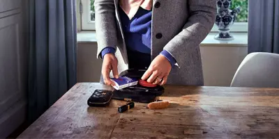 Die Hände einer Frau ordnen ihre Schminksachen und Tempo Taschentücher in einer schwarzen Tasche auf einem Holztisch.