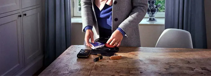 Die Hände einer Frau ordnen ihre Schminksachen und Tempo Taschentücher in einer schwarzen Tasche auf einem Holztisch.