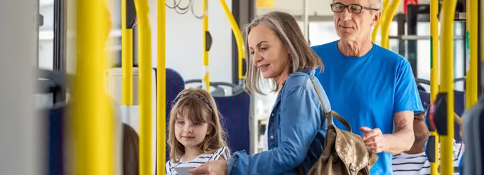 Una bambina e i suoi nonni su un autobus giallo e blu mentre la nonna consulta un foglio di carta.