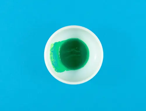 Su uno sfondo blu c'è un contenitore bianco visto dall'alto contenente della pittura verde.