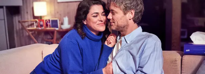 Una coppia di innamorati siede accoccolata su un divano beige in un salotto.