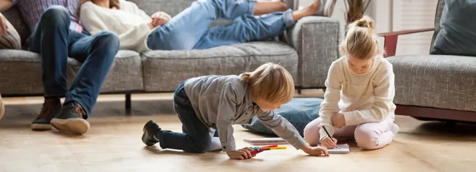 Una coppia di genitori si rilassa sul divano mentre i bambini giocano sul pavimento del salotto.
