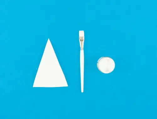 Triangolo di carta e pennello bianchi con un piccolo contenitore con della pittura bianca giacciono su sfond blu.