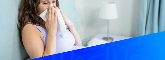 Afbeelding van een vrouw die in bed haar neus zit te snuiten, met daaroverheen een diagonaal blauw Tempo-patroon in de rechterhoek.