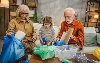 Una bambina che smista i materiali riciclabili con i nonni in un salotto moderno.