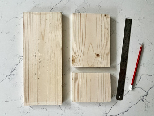 Tre tavole di legno tagliate con righello metallico e matita rossa su sfondo in marmo.