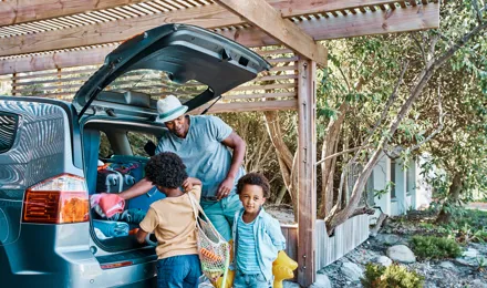 Ein Vater und zwei Kinder packen den Kofferraum ihres Autos für einen Ausflug über das Wochenende.