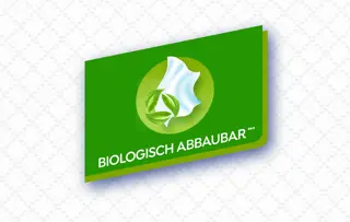 Grünes Etikett mit einem Recyclingsymbol und dem Text „BIOLOGISCH ABBAUBAR“ als Hinweis auf eine biologisch abbaubare Verpackung.