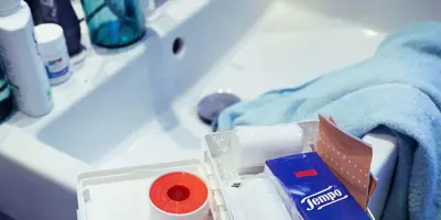 Ein Erste-Hilfe-Kasten in einem Waschbecken mit Tempo Taschentüchern, Scheren und anderen grundlegenden Dingen.