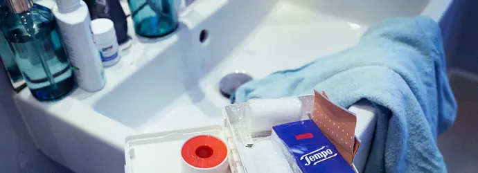 Ein Erste-Hilfe-Kasten in einem Waschbecken mit Tempo Taschentüchern, Scheren und anderen grundlegenden Dingen.