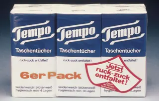 Een vintage sixpack Tempo zakdoekjes in een blauw-witte verpakking, afgebeeld tegen een blauw-witte achtergrond met kleurverloop.