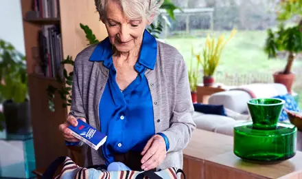 Eine ältere Dame hält eine Packung Tempo Taschentücher über einer gestreiften Handtasche, um sie einzupacken.
