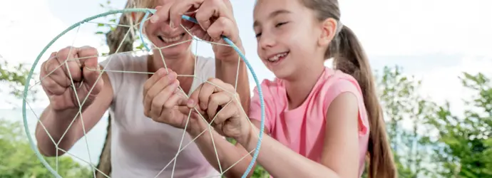 Eine Frau und ein Mädchen basteln zusammen einen bunten Traumfänger.