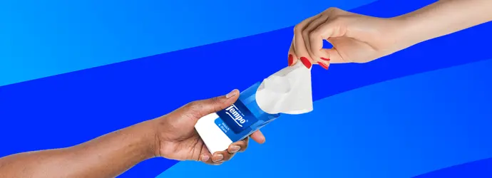Zwei Hände tauschen eine Tempo Taschentuch Packung vor einem blau gestreiften Hintergrund aus