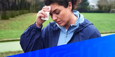 Afbeelding van een vrouw die haar bezwete voorhoofd afveegt over een diagonaal Tempo blauw patroon in de rechterhoek.