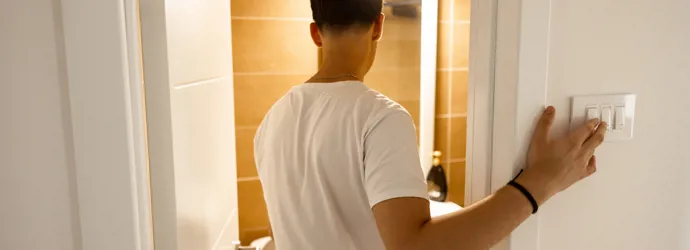 Un uomo con t-shirt bianca entra in un bagno e accende le luci.