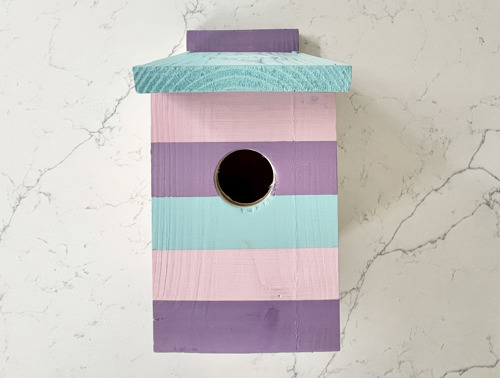 Casetta per uccelli finita dipinta con strisce pastello e foro d’ingresso rotondo.