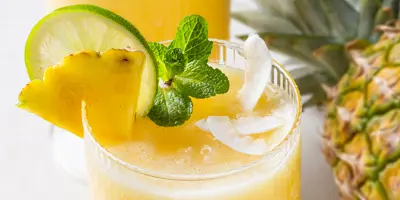 Ein erfrischendes, eisgekühltes Ananasgetränk im Glas mit Ananas, Limette und Minze garniert.