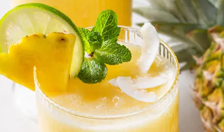 Ein erfrischendes, eisgekühltes Ananasgetränk im Glas mit Ananas, Limette und Minze garniert.