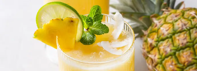 Ein erfrischendes, eisgekühltes Ananasgetränk im Glas mit Ananas, Limette und Minze garniert.