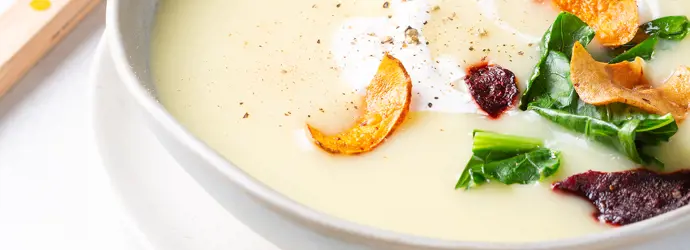 Cremige Kohlrabi Suppe in einer hellen Schale, garniert mit Gemüsechips, Crème fraîche und gemahlenem Pfeffer.