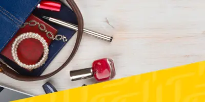 Una borsa blu è aperta su un tavolo con gioielli, smalto rosso e una penna d'argento accanto.