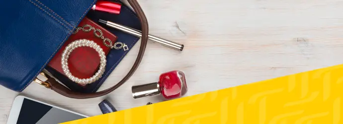 Una borsa blu è aperta su un tavolo con gioielli, smalto rosso e una penna d'argento accanto.