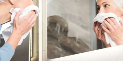 Frau mit kurzen, weißen Haaren sieht sich und ihre trändenden Augen im Badezimmerspiegel an