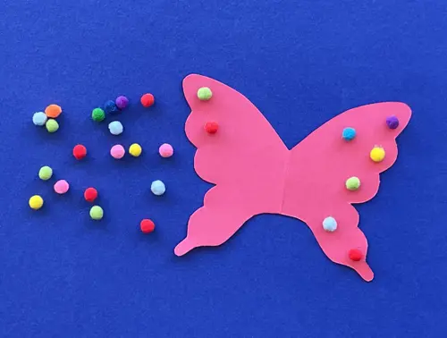 Ali di farfalla rosa con palline di carta colorate su sfondo blu. Sulla sinistra delle palline di carta colorate.