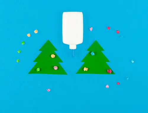 Due ritagli a forma di albero natalizio e al centro un dispenser bianco, circondati da piccoli pezzetti di carta colorati.