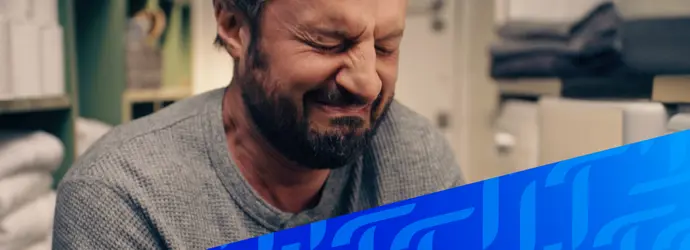 Ein Mann mit Bart sitzt in seinem Badezimmer und weint in ein Tempo-Taschentuch. Das Bild wird von einem diagonalen blauen Tempo-Muster in der rechten unteren Ecke überlagert.