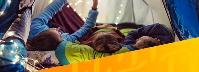 Bild von drei Personen, die in einem Zelt mit Lichtern liegen, überlagert von einem diagonalen gelben Tempo-Muster in der rechten Ecke.