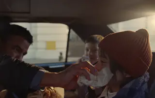 Ein Mann beugt sich über die Rücklehne eines Taxisitzes, um einem kleinen Jungen zu helfen, sich mit einem Tempo Taschentuch die Nase zu putzen