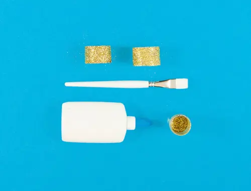 Un contenitore di plastica e un pennello bianchi su uno sfondo blu con un contenitore e un nastro adesivo glitterato oro.