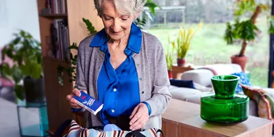 Eine ältere Dame hält eine Packung Tempo Taschentücher über einer gestreiften Handtasche, um sie einzupacken.